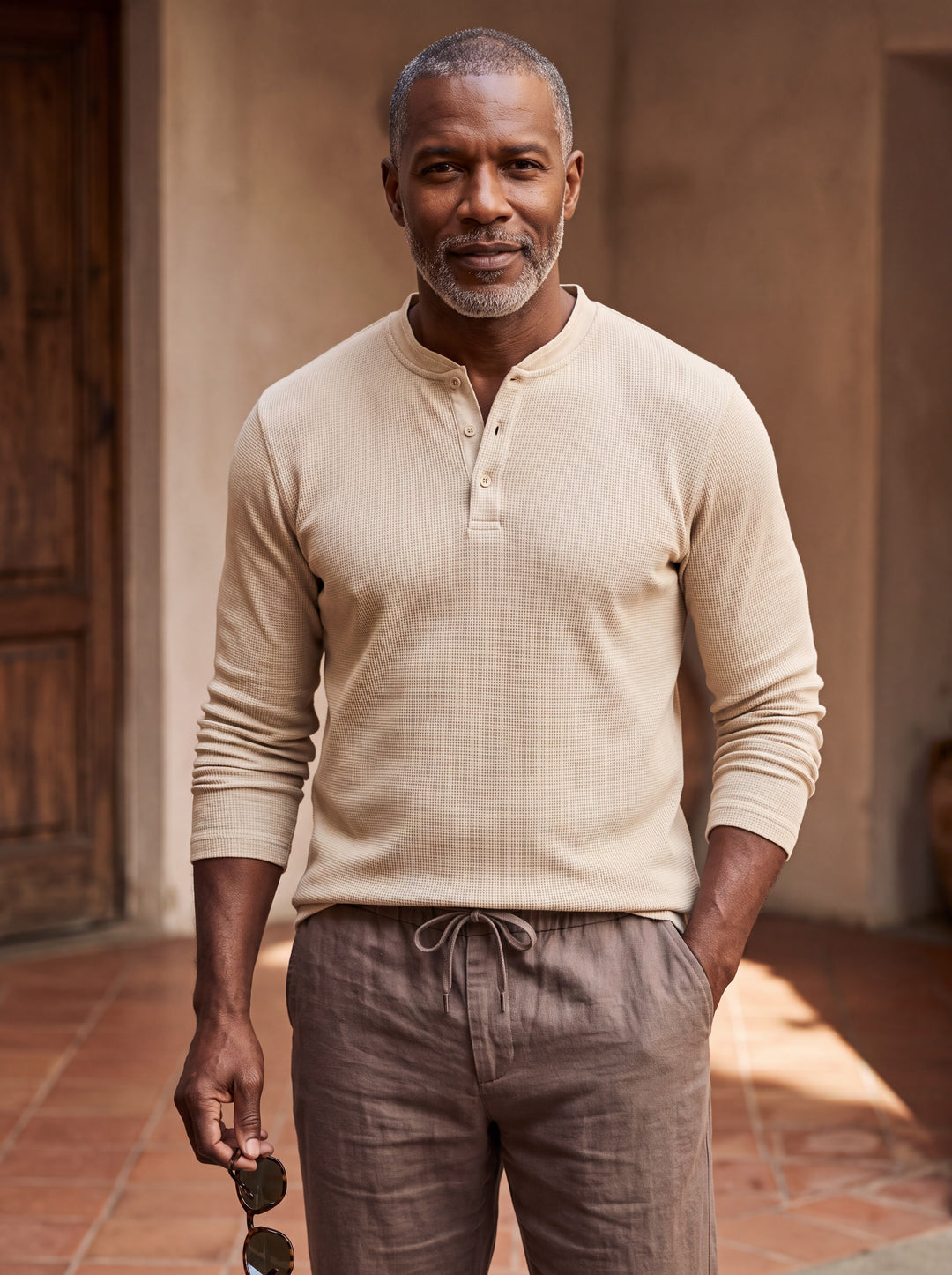 Cyrus Men henley shirt in sand, worn by a model on a Mediterranean terrace - Gentlemens Manor lifestyle