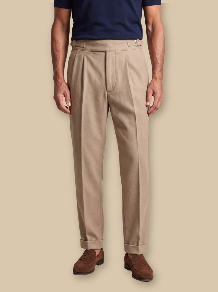 Reuben trousers in Sand, worn by a model on a warm sand studio background - Gentlemens Manor