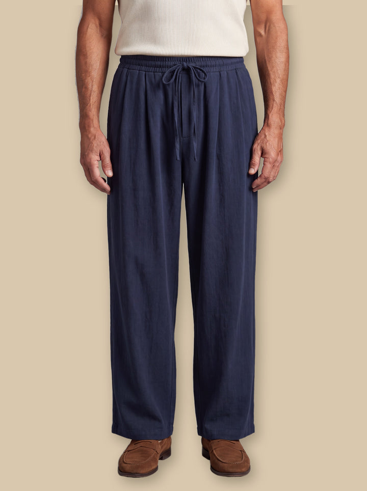 Riley trousers in Navy, worn by a model on a warm sand studio background - Gentlemens Manor