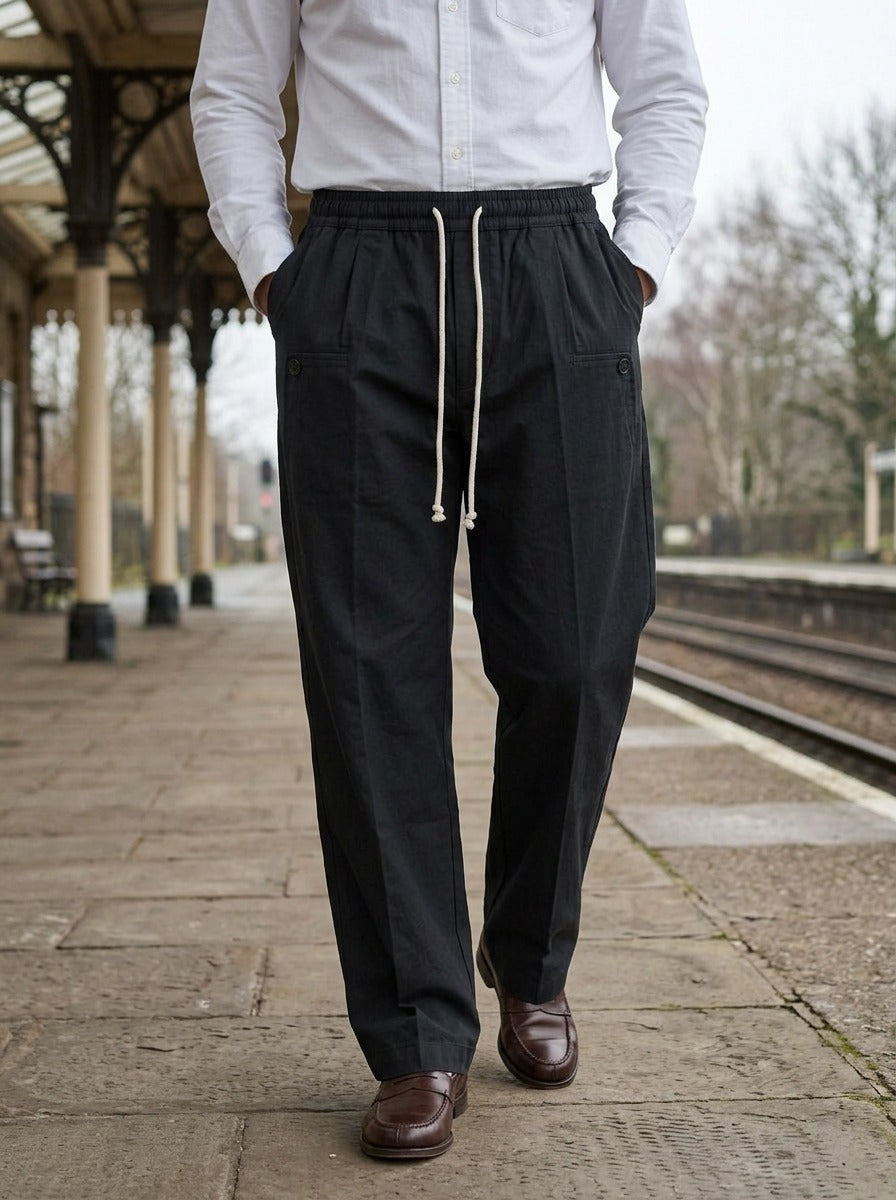 Sedley pleated drawstring crease trousers in Black, lifestyle on a railway platform, Gentlemens Manor