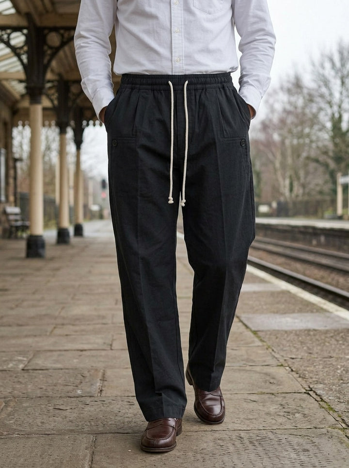 Sedley pleated drawstring crease trousers in Black, lifestyle on a railway platform, Gentlemens Manor
