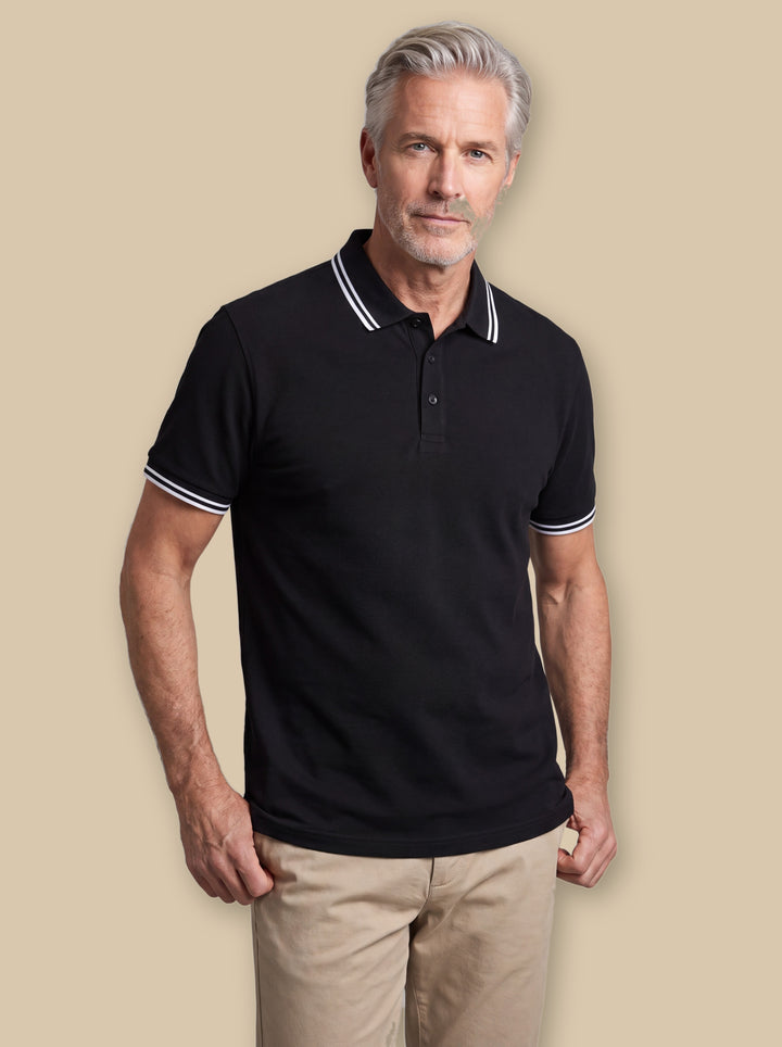 Walter polo shirt in Black, worn by a model on a warm sand studio background - Gentlemens Manor